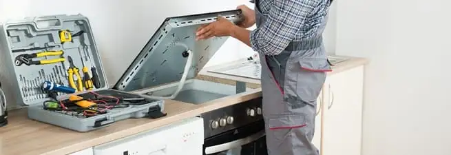 Cooktop repair technician lifting a built-in stovetop for service in Grand Rapids, MI