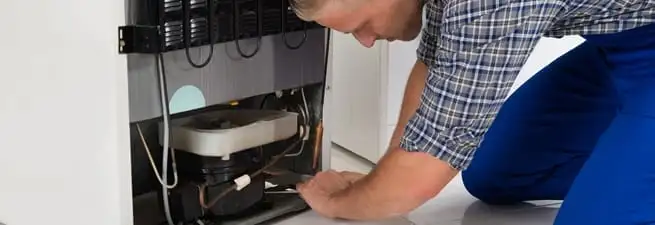 Refrigerator repair technician servicing the compressor and condenser area in Grand Rapids, MI
