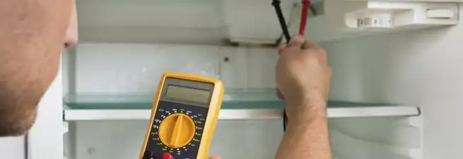 Refrigerator repair technician testing electrical components with a multimeter in Grand Rapids, MI