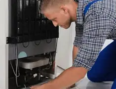 Refrigerator repair technician servicing the compressor and condenser area in Grand Rapids, MI