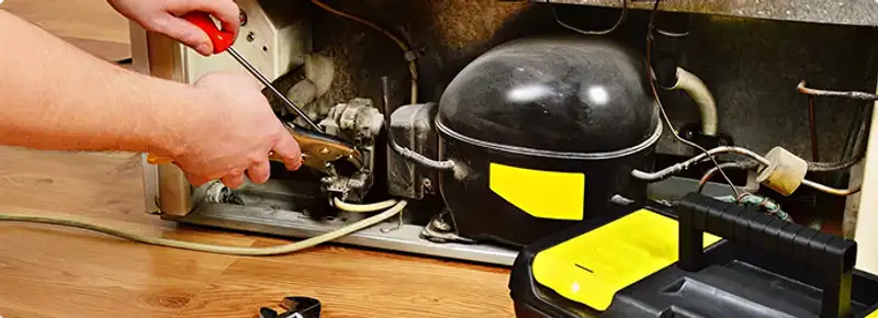 Refrigerator repair technician fixing the compressor and wiring in Grand Rapids, MI
